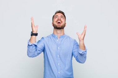 Genç adam mutlu, şaşkın, şanslı ve şaşırmış hissediyor, zaferi kutluyor, iki eli havada.