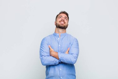 Genç adam kollarını kavuşturup mutlu bir şekilde gülüyor, rahat, pozitif ve tatmin olmuş bir şekilde.