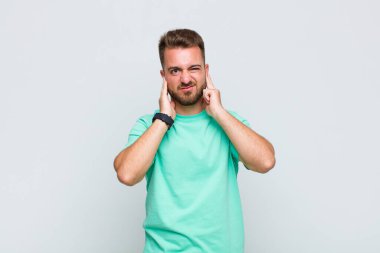 Genç adam sinirli, stresli ve sinirli görünüyor, iki kulağını da sağır edici bir ses, ses ya da yüksek sesle kapatıyor.