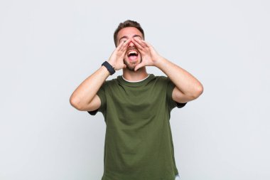 Genç adam mutlu, heyecanlı ve pozitif hissediyor. Elleri ağızda, bağırıyor.