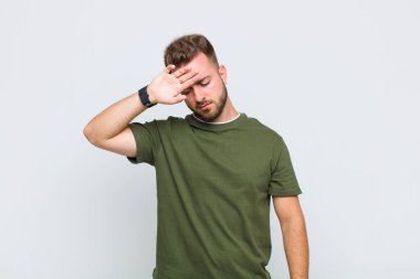 Genç adam stresli, yorgun ve hayal kırıklığına uğramış görünüyor, alnından ter damlıyor, umutsuz ve bitkin hissediyor.