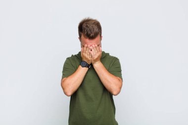 Genç adam üzgün, hayal kırıklığına uğramış, gergin ve depresif, iki eliyle yüzünü kaplayan, ağlayan