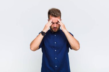 Genç adam stresli ve hayal kırıklığına uğramış görünüyor, baskı altında çalışıyor, başı ağrıyor ve sorunlarla boğuşuyor.