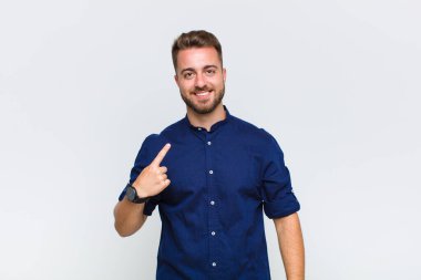 Genç adam gururlu, kendinden emin ve mutlu görünüyor, gülümsüyor ve kendini işaret ediyor veya bir numaralı işareti yapıyor.