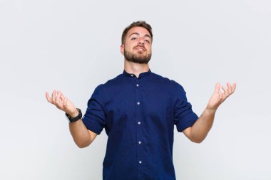 young man shrugging with a dumb, crazy, confused, puzzled expression, feeling annoyed and clueless