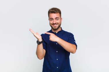 Genç adam neşeyle gülümsüyor ve bir objeyi göstererek veya reklamını yaparak avucundaki kopyalama alanını işaret ediyor.