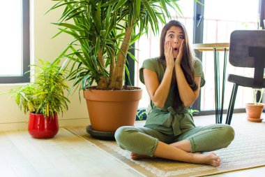 Güzel kadın şok olmuş ve korkmuş hissediyor, ağzı açık ve elleri yanaklarında korkmuş görünüyor.