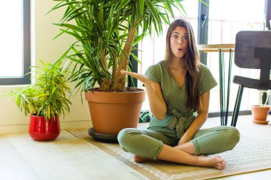 Güzel bir kadın şaşırmış ve şoka uğramış görünüyor, çenesi düşmüş, elinde açık bir elle bir nesne tutuyor.