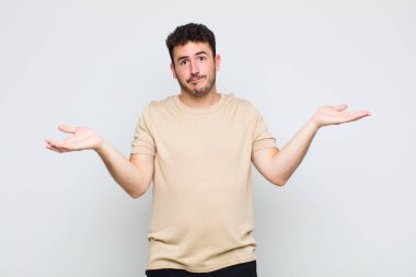 Genç adam şaşkın, şaşkın ve stresli görünüyor, farklı seçenekler arasında merak ediyor, kararsız hissediyor.