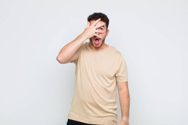 Genç adam şok olmuş, korkmuş ya da korkmuş görünüyor. Yüzü elle örtülmüş ve parmaklarının arasından gizlice bakıyor.