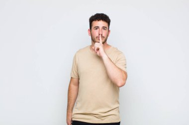 Genç adam ciddi görünüyor ve parmaklarını dudaklarına bastırıp sessizlik ya da sessizlik talep ediyor, sır saklıyor.