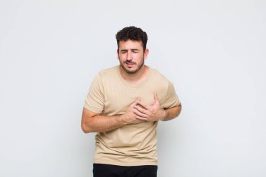 Genç adam üzgün, yaralı ve kalbi kırık görünüyor, iki elini de kalbe yakın tutuyor, ağlıyor ve bunalımda.