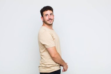 Genç adam neşeyle gülümsüyor, mutlu, tatmin olmuş ve rahatlamış hissediyor, kollarını kavuşturup yan tarafa bakıyor.