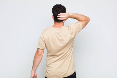 Genç adam düşünüyor ya da şüphe ediyor, kafasını kaşıyor, kafası karışık ve kafası karışık hissediyor, geriye ya da arkaya bakıyor.