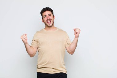 Genç adam son derece mutlu ve şaşırmış görünüyor, başarıyı kutluyor, bağırıyor ve zıplıyor.