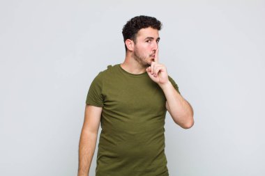 Genç adam sessizlik ve sessizlik istiyor, parmaklarıyla ağzının önünde işaret ediyor, 