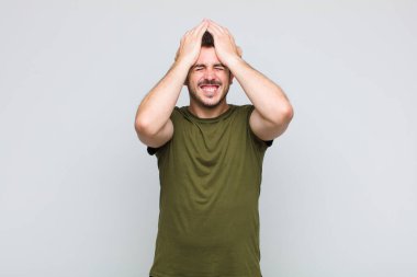 Genç adam stresli ve endişeli, depresif ve hayal kırıklığına uğramış hissediyor, iki elini de başa kaldırıyor.