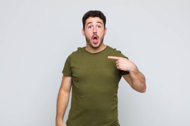 Şok olmuş ve ağzı açık, kendini işaret eden genç bir adam.