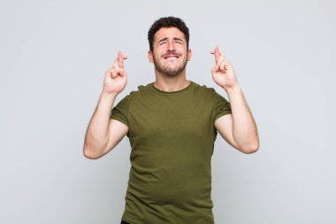 Genç adam gülümsüyor ve endişeyle iki parmağını çapraz yapıyor. Endişeli ve iyi şanslar diliyor.