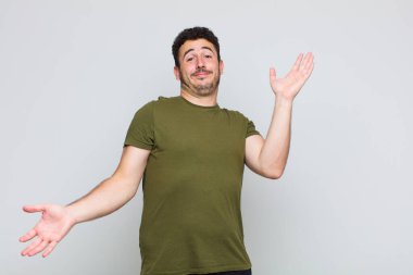 young man shrugging with a dumb, crazy, confused, puzzled expression, feeling annoyed and clueless