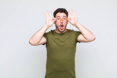 Genç adam şaşkın, şaşırmış ve şaşırmış hissediyor. Elinde şaşkın, inançsız bir bakışla gözlük tutuyor.