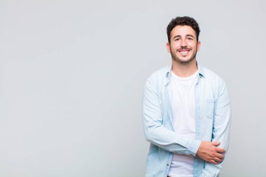 Genç adam utangaç ve neşeli bir şekilde gülüyor, arkadaş canlısı ve olumlu ama güvensiz bir tavırla.