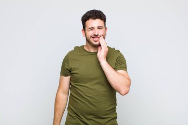 Yanak tutan ve acı çeken diş ağrısı çeken genç adam hasta, sefil ve mutsuz hisseden, dişçi arayan.