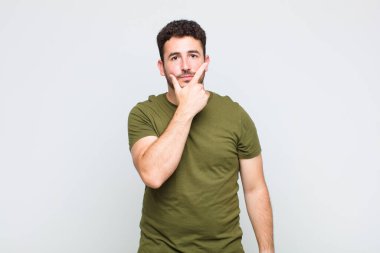 Genç adam ciddi görünüyor, düşünceli ve güvensiz, bir kolu çapraz ve çene üzerinde, seçenekleri tartıyor