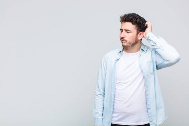 Genç adam şaşkın ve şaşkın hissediyor, başını kaşıyor ve yana bakıyor.