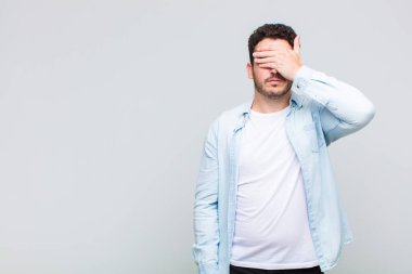 Genç adam tek eliyle gözlerini kapatıyor. Korkmuş ya da endişeli, merak ediyor ya da körü körüne bir sürpriz bekliyor.