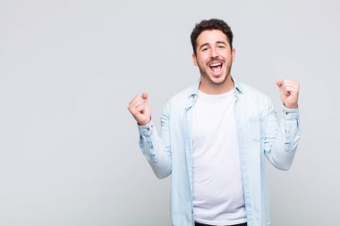 Genç adam son derece mutlu ve şaşırmış görünüyor, başarıyı kutluyor, bağırıyor ve zıplıyor.