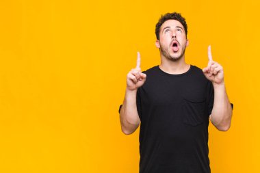 Genç adam şaşırmış, şaşırmış ve ağzı açık bir şekilde iki eliyle uzayı göstererek uzayı kopyalıyor.