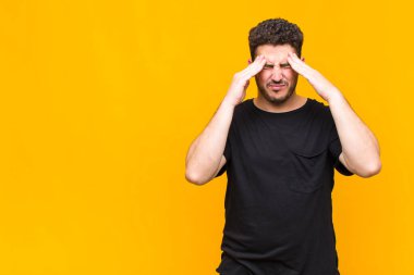 Genç adam stresli ve hayal kırıklığına uğramış görünüyor, baskı altında çalışıyor, başı ağrıyor ve sorunlarla boğuşuyor.