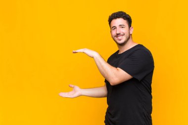 Delikanlı iki eli yanda olan bir objeyi tutuyor fotokopi alanı, bir nesneyi gösteriyor, sunuyor ya da reklamını yapıyor.