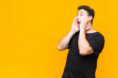 Genç adam mutlu, heyecanlı ve şaşırmış hissediyor, iki eli yüzü yana bakıyor.