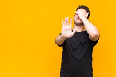 Genç adam yüzünü eliyle kapatıyor ve kamerayı durdurmak için diğer elini öne koyuyor, fotoğraf ya da resimleri reddediyor.