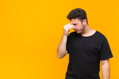 Genç adam stresli, mutsuz ve hayal kırıklığına uğramış, alnına dokunuyor ve şiddetli baş ağrısı çekiyor.