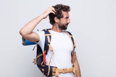 Genç adam şaşkın ve şaşkın hissediyor, başını kaşıyor ve yana bakıyor.