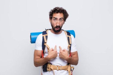 Genç adam şaşkın ve şaşkın bir bakışla kendini işaret ediyor. Seçildiğine şaşırmış ve şaşırmış.