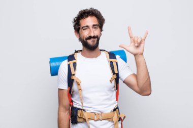 Genç adam mutlu, eğlenceli, kendinden emin, pozitif ve asi hissediyor, elle kaya veya heavy metal işareti yapıyor.