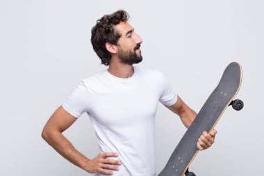 Genç adam mutlu, neşeli ve kendinden emin görünüyor, gururla gülümsüyor ve iki elini de kalçasında istiyor.