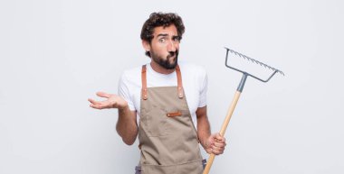 Genç adam şaşkın, şaşkın ve stresli görünüyor, farklı seçenekler arasında merak ediyor, kararsız hissediyor.