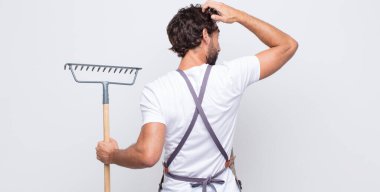 Genç adam bilgisiz ve kafası karışık, bir çözüm düşünüyor, eli kalçasında, diğeri kafasında, dikiz aynasından.