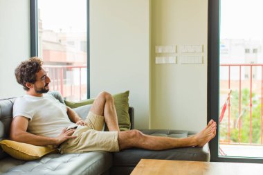 Genç adam mutlu, neşeli ve kendinden emin görünüyor, gururla gülümsüyor ve iki elini de kalçasında istiyor.