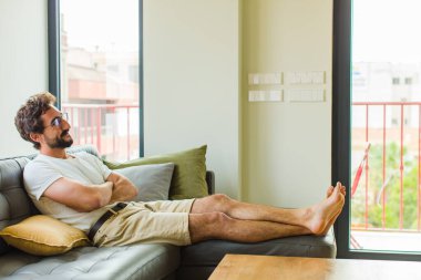 Genç adam mutlu, gururlu ve umutlu, merak ediyor ya da düşünüyor, çapraz kollarla uzayı taklit ediyor.