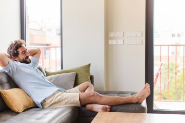 Genç adam gülümsüyor ve rahatlıyor, tatmin oluyor, kaygısız, neşeli ve rahatlatıcı.