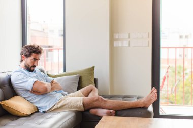 Genç adam mutsuz ve hayal kırıklığına uğramış, ciddi görünüyor, sinirlenmiş ve kollarını kavuşturmuş.