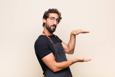 Delikanlı iki eli yanda olan bir objeyi tutuyor fotokopi alanı, bir nesneyi gösteriyor, sunuyor ya da reklamını yapıyor.