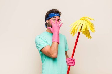 Genç adam elleriyle yüzünü kapatıyor, parmaklarının arasından şaşkın bir ifadeyle yan tarafa bakıyor.