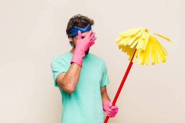 Genç adam stresli, utanmış ya da üzgün görünüyor, baş ağrısı var, yüzü elle kapatılmış.